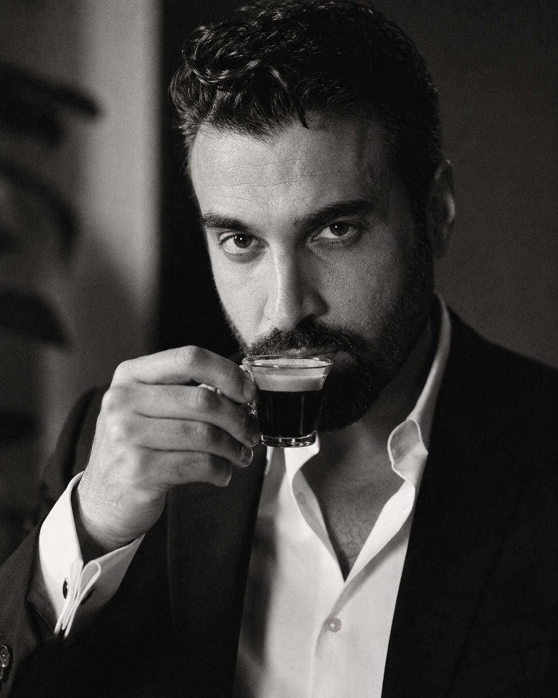 A.J. Castro in a dark suit, sipping espresso, black and white portrait